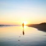 silhouette of boy running in body of water during sunset